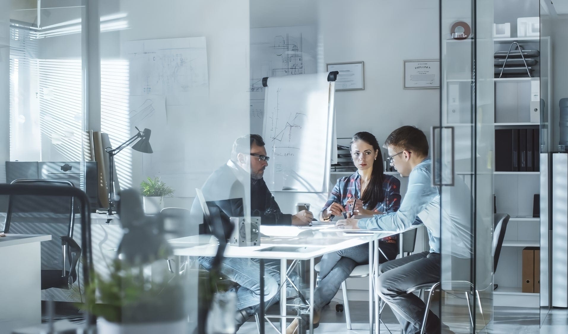 Three colleagues meeting around a table in a glass-walled office