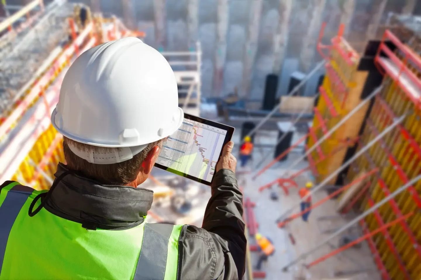 Construction professional in a hard hat reviewing a schedule on a tablet at a job site