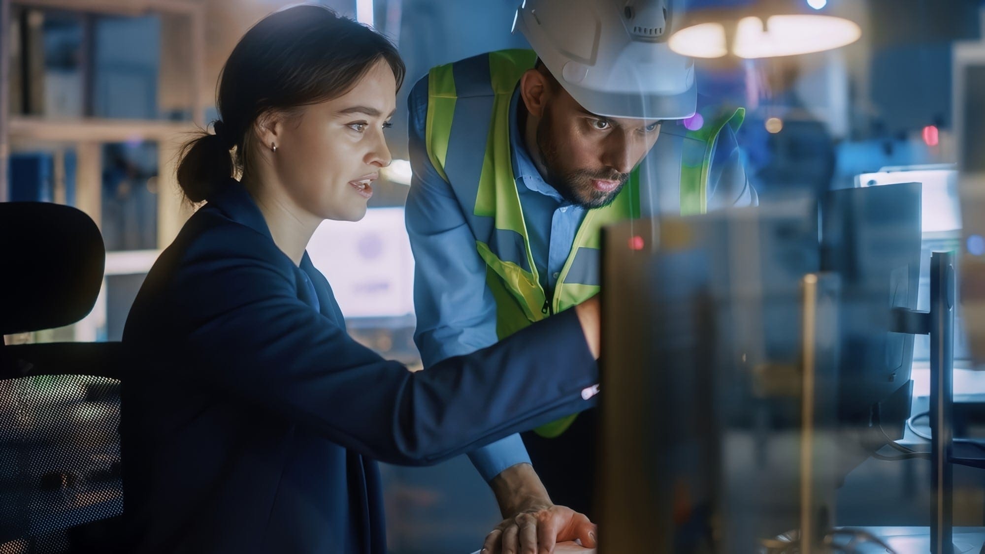 Engineer and site worker in a safety vest reviewing project data on a monitor together